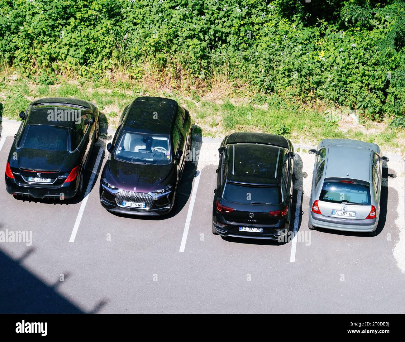 Strasbourg, France - Jun 5, 2023: A variety of cars - Renault, VW, SUV, estate wagons, Citroen, and DS models - stand parked in a row, set against a backdrop of towering bushes Stock Photo