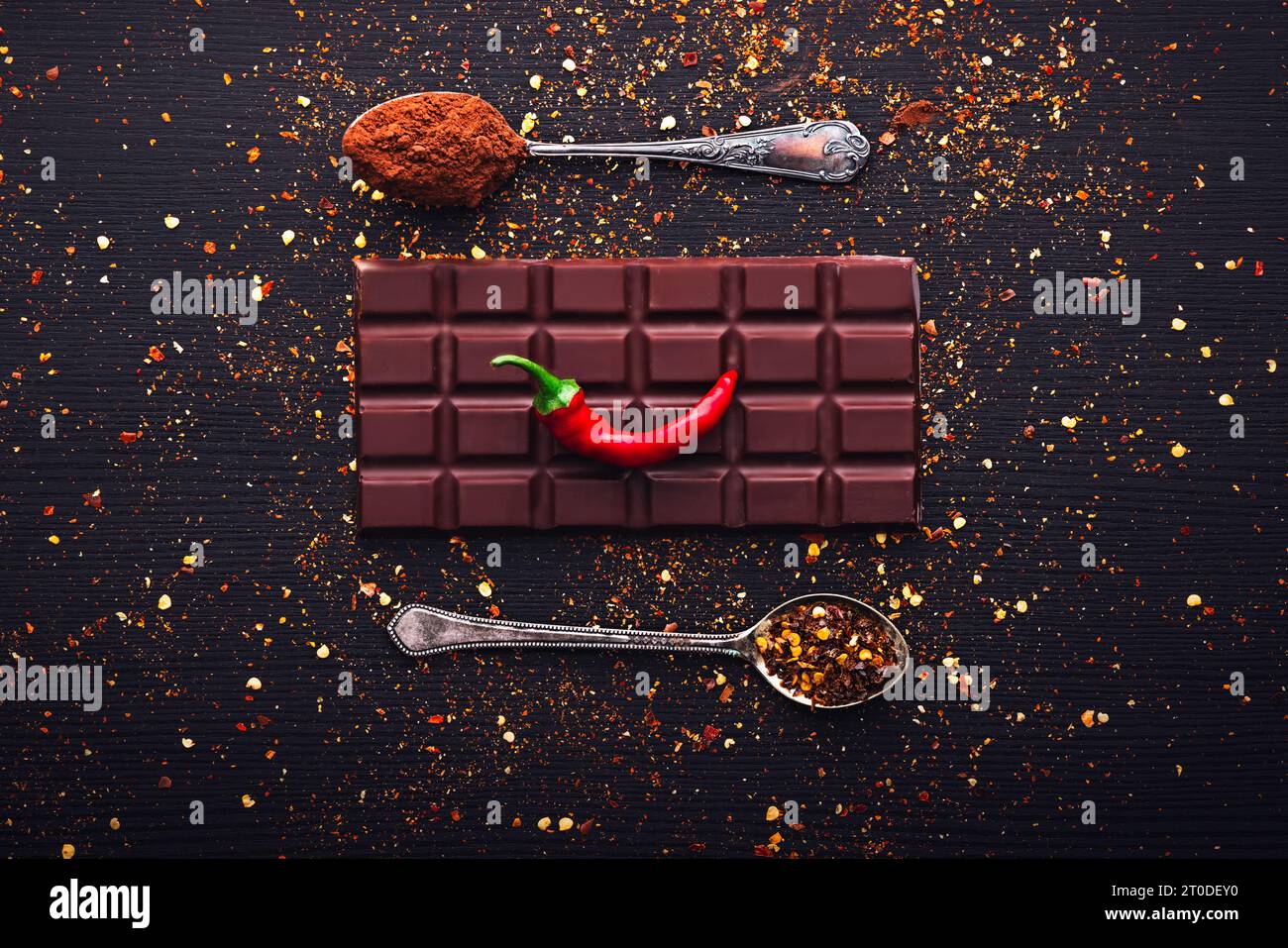 Dark chocolate bar, red hot chilli pepper cayenne,  dry hot chili spices, cocoa beans nibs powder, food tasty design on black wooden background Stock Photo