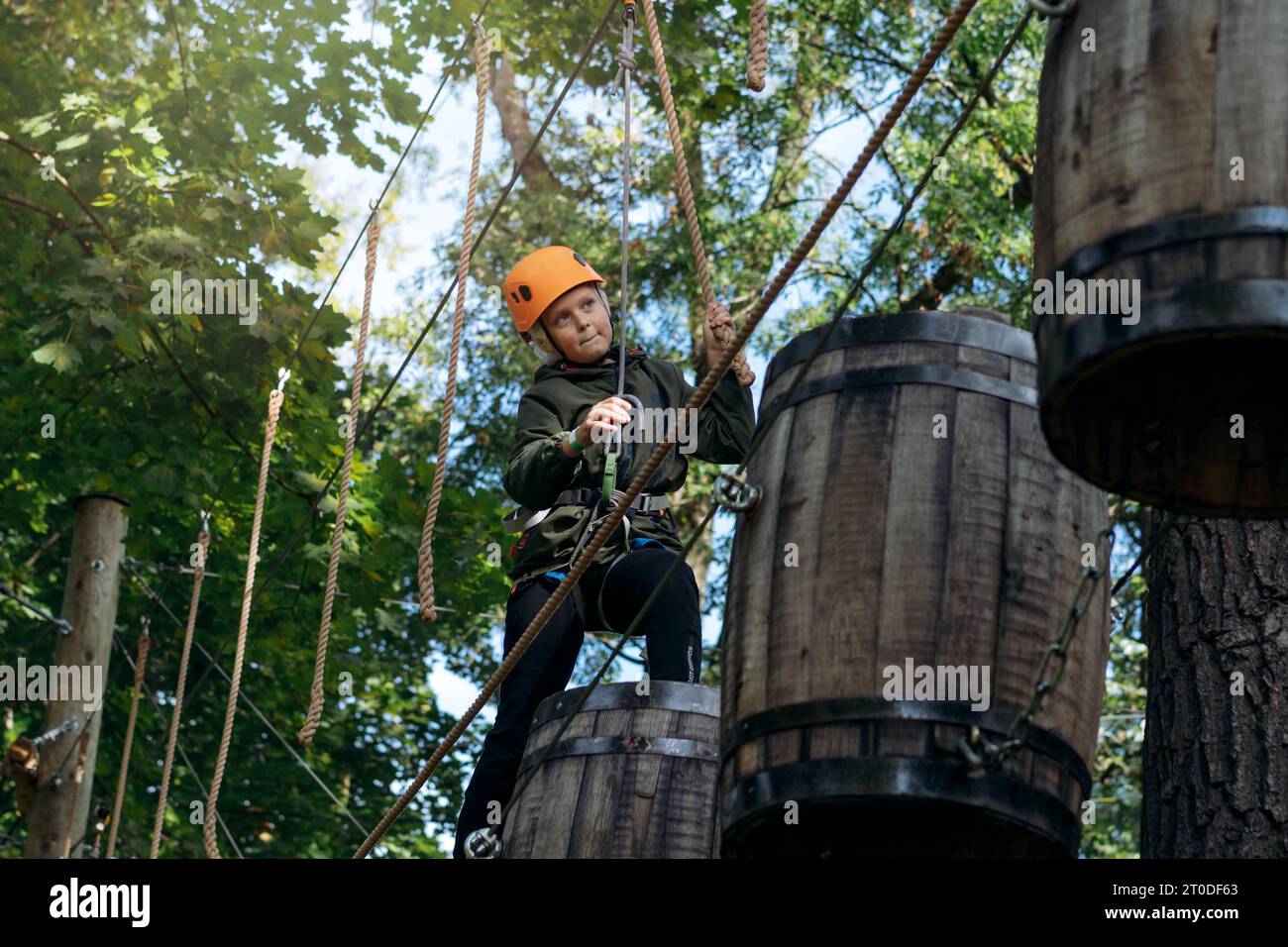 well equipped teenage boy in outdoor passing obstacle course. Active recreation in high rope park Stock Photo