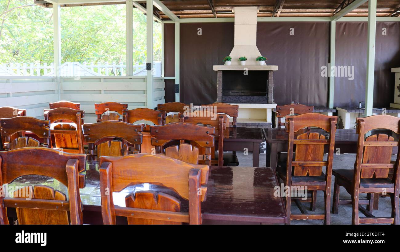 rural cafe with wooden lacquered beautiful furniture and a white fireplace near the wall, interior of a deserted rural restaurant on a covered terrace Stock Photo