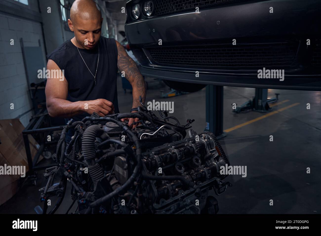 Masculine African American auto-mechanic standing near big black engine ...