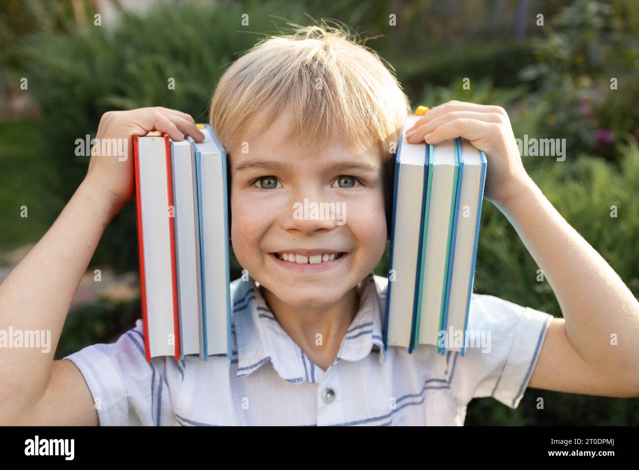 cute joyful 7 year old boy holds several books on shoulders near his