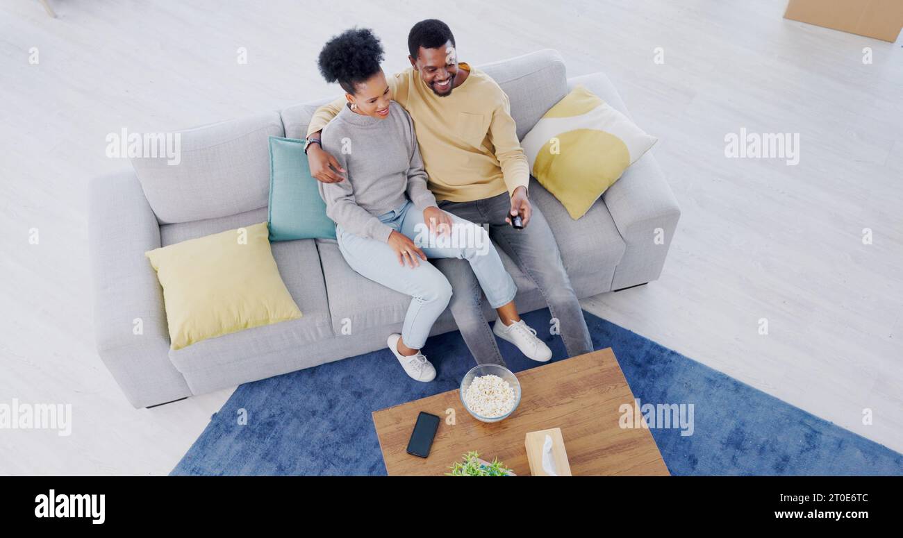 Black couple, top view and couch in living room, tv and relax with popcorn, movies and funny comedy. Man, woman and hug for bonding together Stock Photo