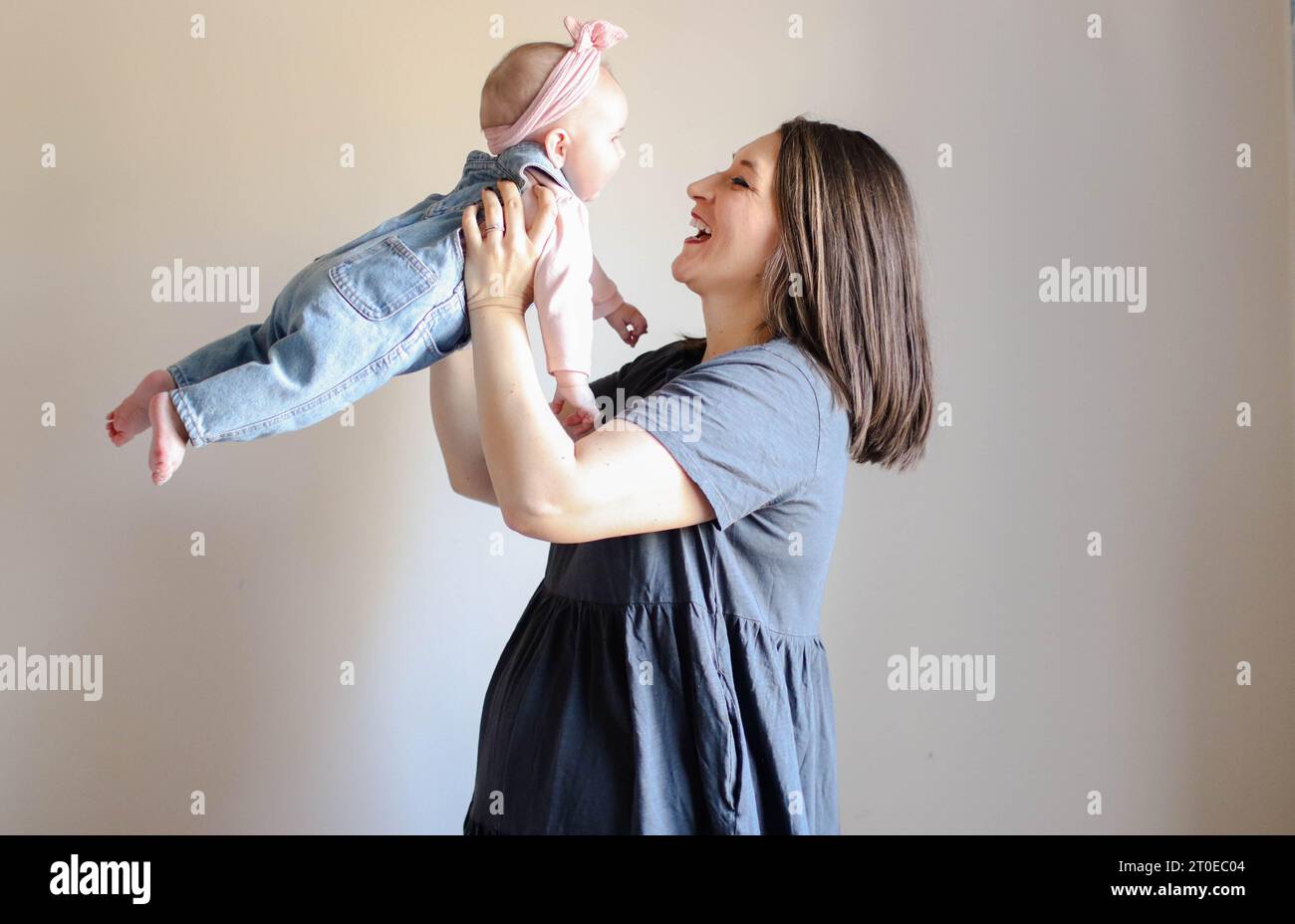 A young woman is joyfully embracing a young toddler, lifting them in the air with both hands in a show of love and affection Stock Photo