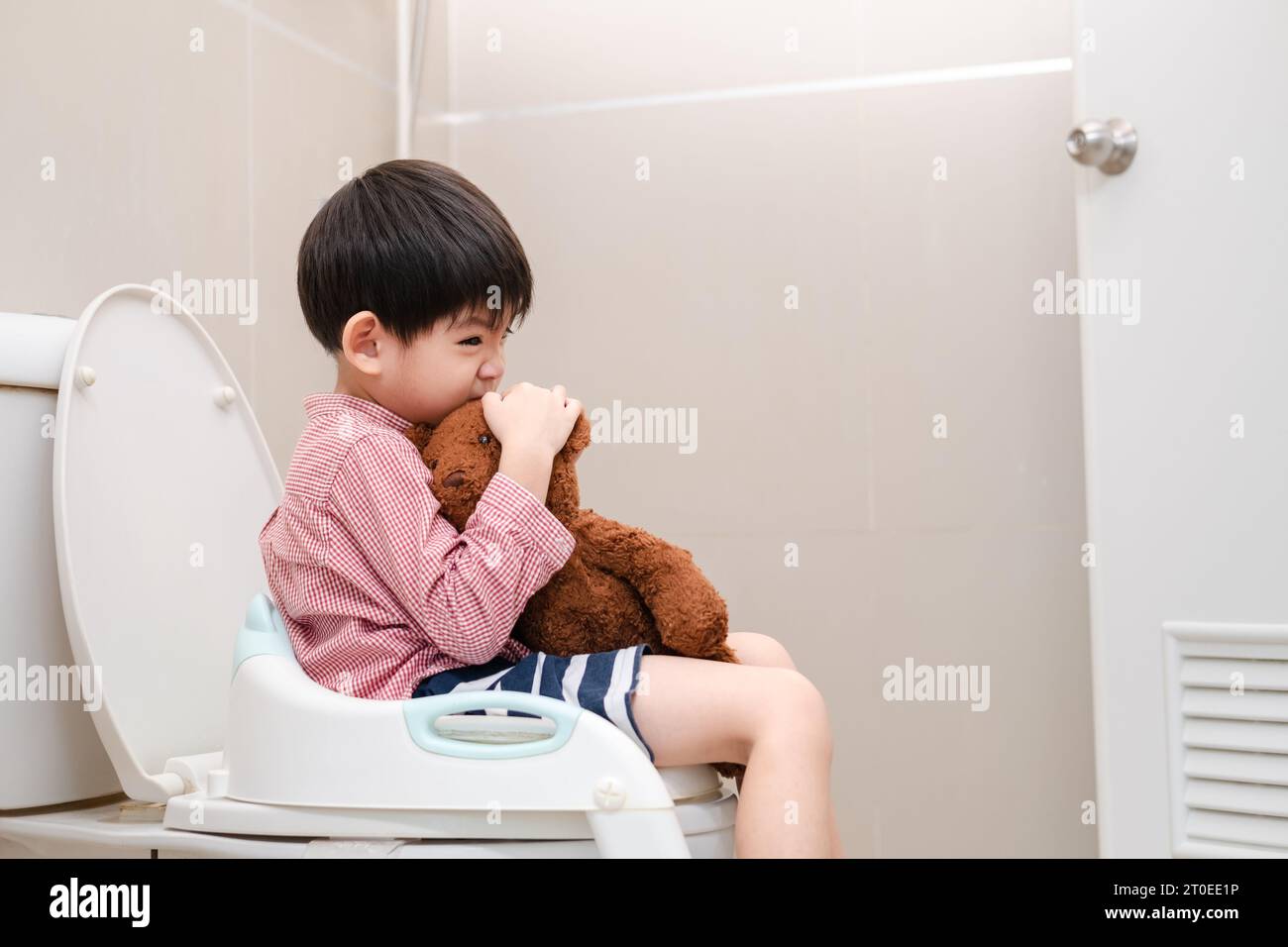 Asian boy Sitting on the toilet bowl in hand holding teddy bear Stock Photo