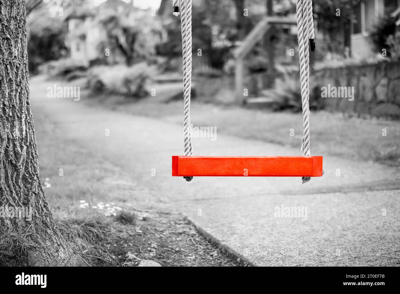 Red swing set with defocused grey scale sidewalk and residential