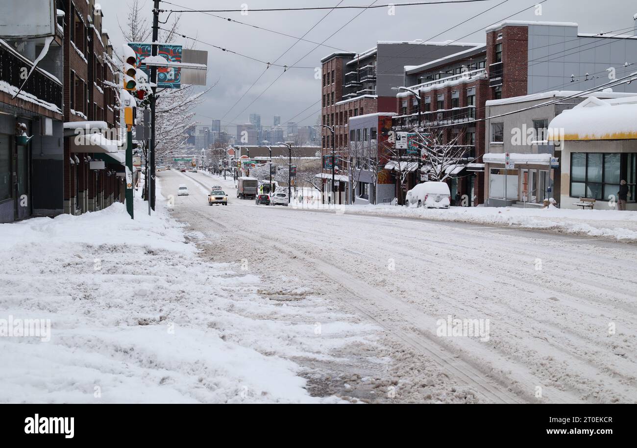 Snow covered city road after snow storm event. Main road not serviced or plowed. Slow traffic is coming up a hill with slush and ice. East Hastings St Stock Photo