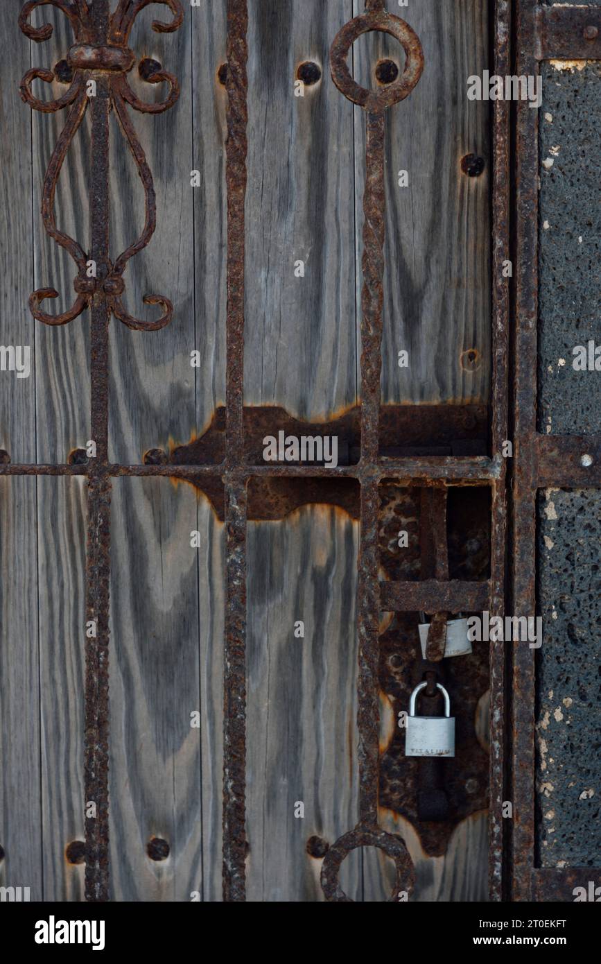 Detail of dilapidated wooden door behind bars, locked with padlocks Stock Photo