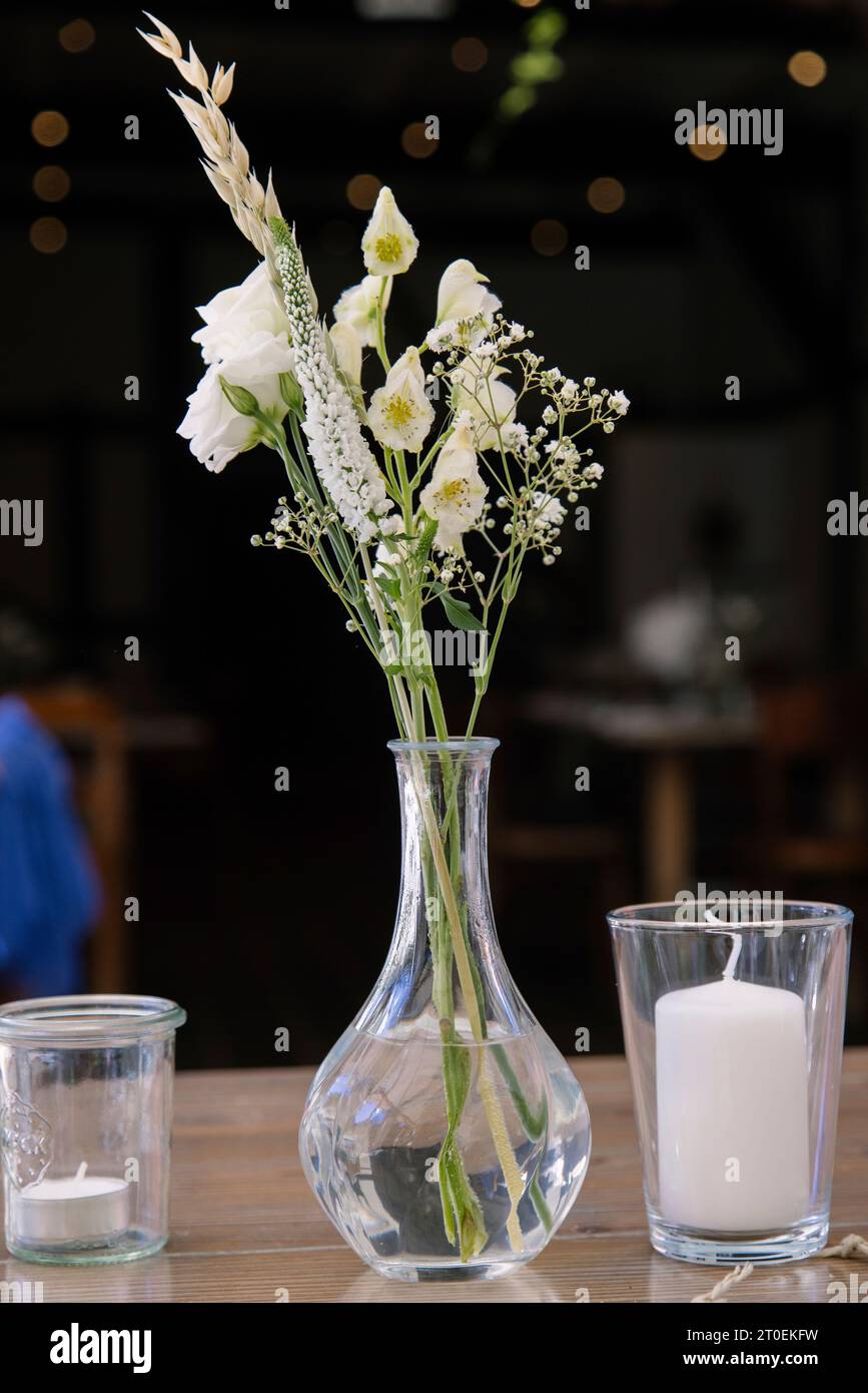Small glass vase with white flowers on a wooden table Stock Photo