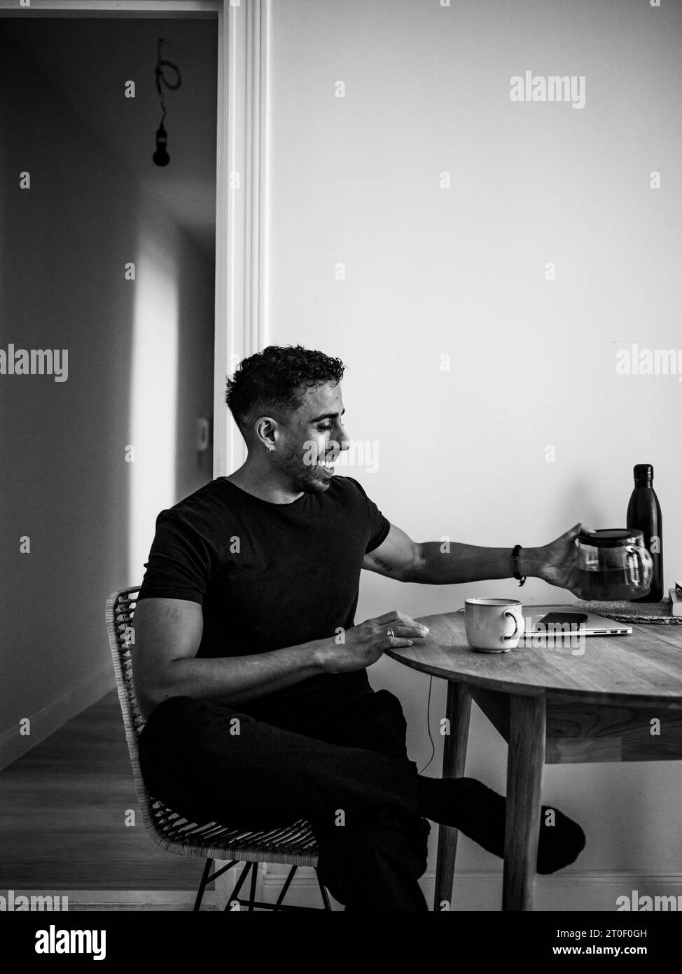 Non-binary person with black t-shirt sits at kitchen table Stock Photo