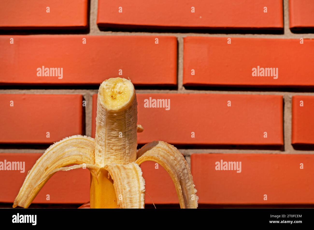 bitten piece of peeled ripe banana from the peel against a brick wall background Stock Photo