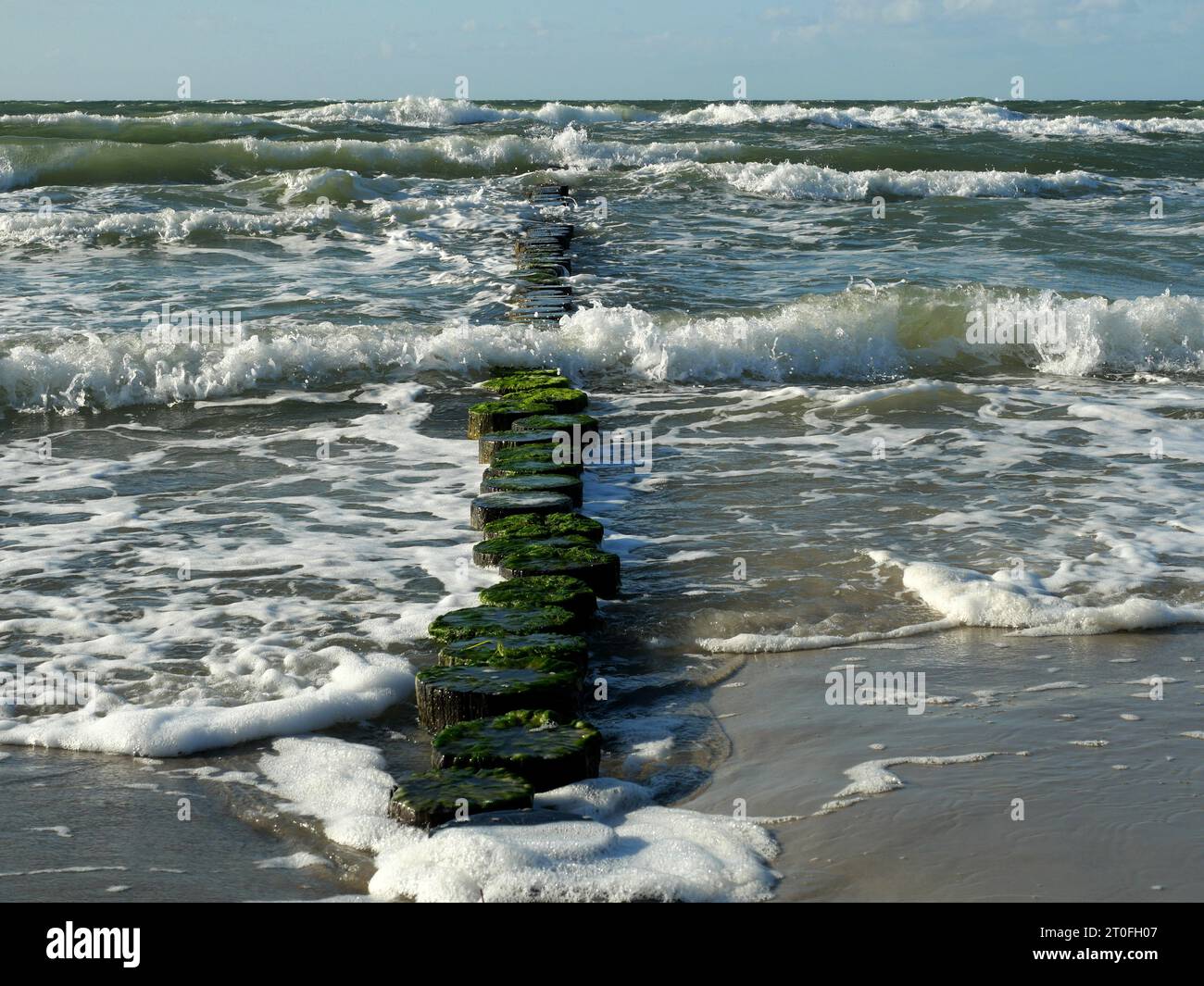 Beach of Ahrenshoop in stormy weather and sunshine. High waves are broken by groynes. Stock Photo