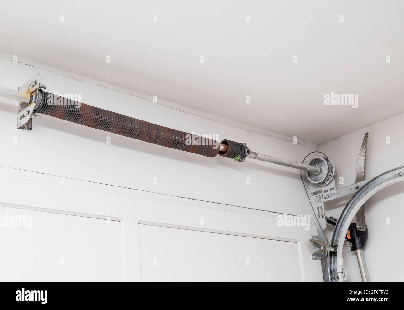 Broken garage door spring or torsion spring from overhead sectional door inside white garage. Sheared-off spring has reached lifespan cycles or materi Stock Photo