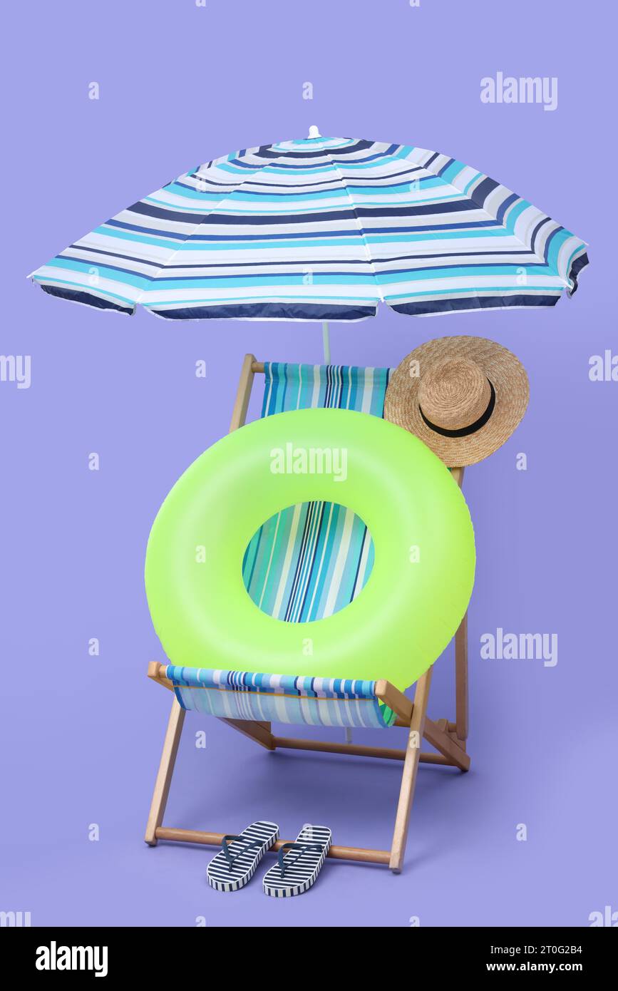 Deck chair, umbrella and other beach accessories on purple background ...