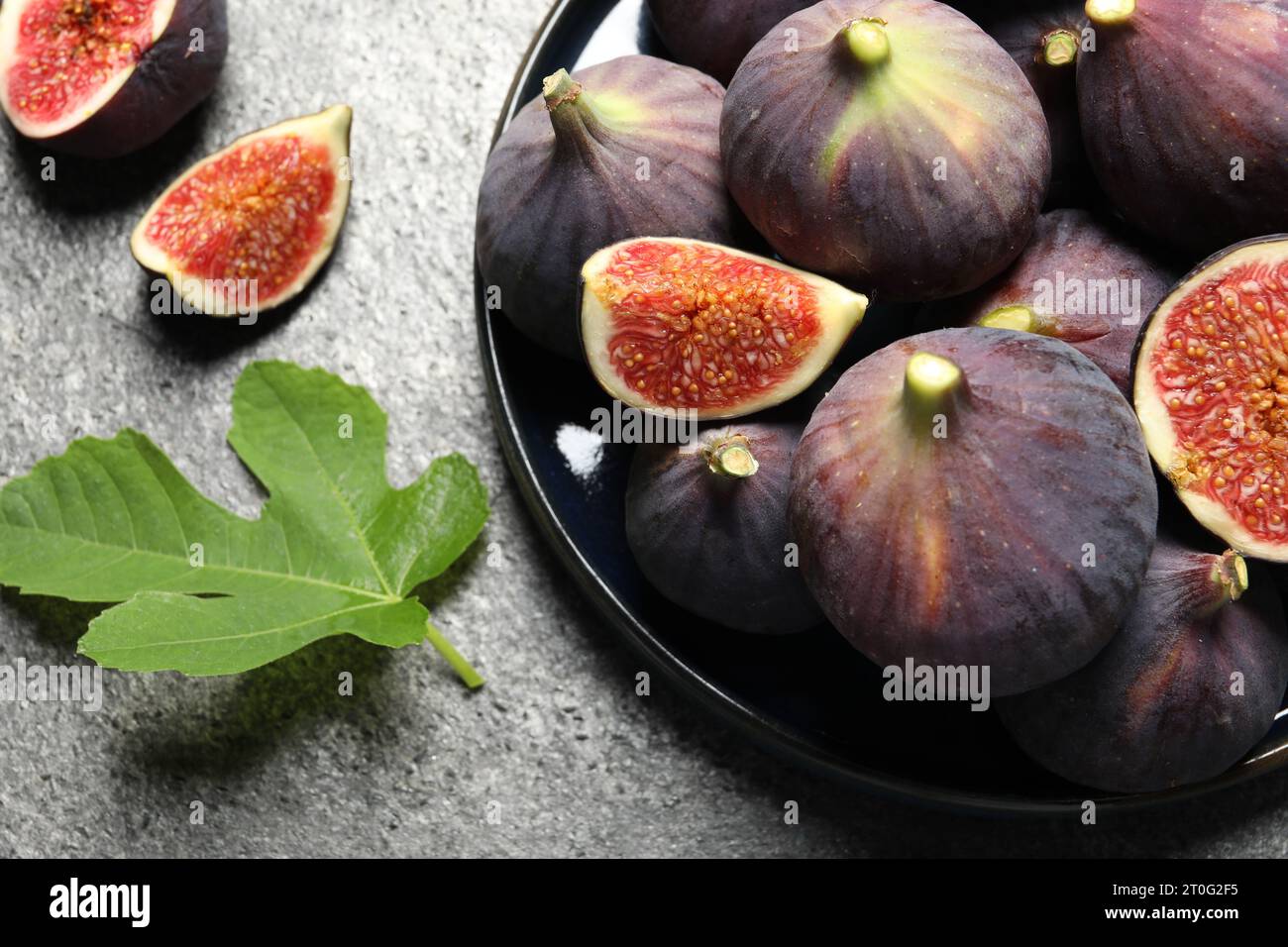 Whole and cut ripe figs with leaf on light grey textured table, flat ...
