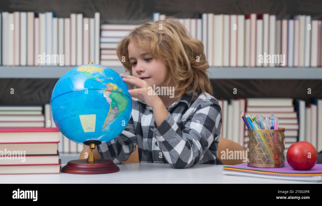 School pupil looking at globe in library at the elementary school. World globe. Kid boy from elementary school with book. Concept of education and lea Stock Photo