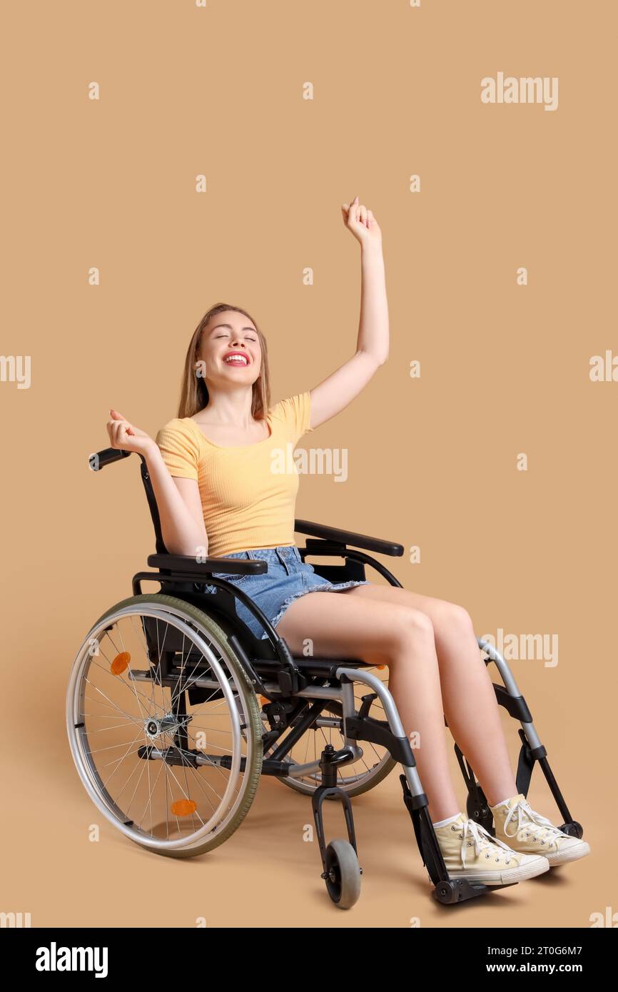 Happy young woman in wheelchair on beige background Stock Photo - Alamy