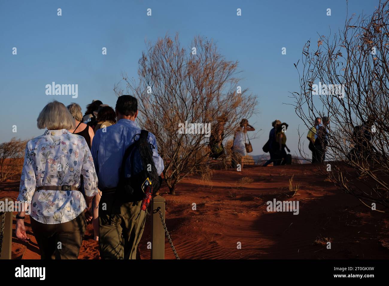 Guests walking up a low red sand dune, arriving at the Uluru sunset ...