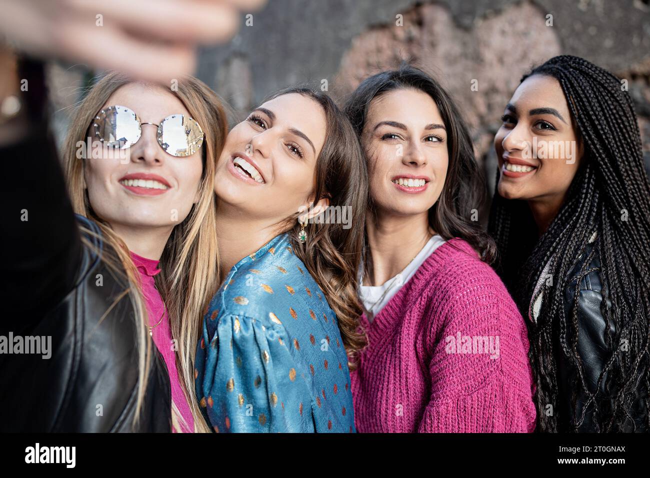 Four vibrant young women are capturing a joyful selfie moment in the historic part of the city, their smiles radiating happiness. Stock Photo