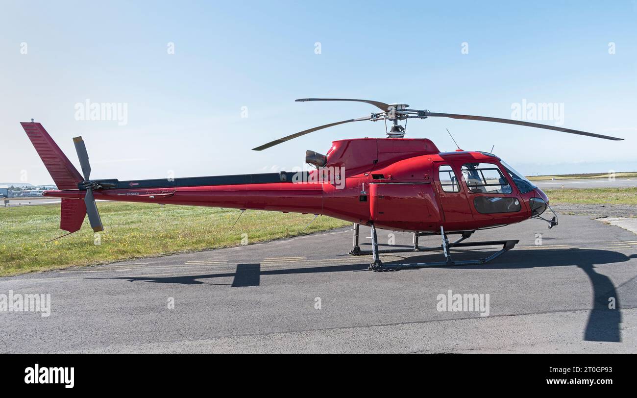 small red tourist helicopter sitting on the ground at an airport with a clear blue sky in the background and tarmac in the foreground Stock Photo