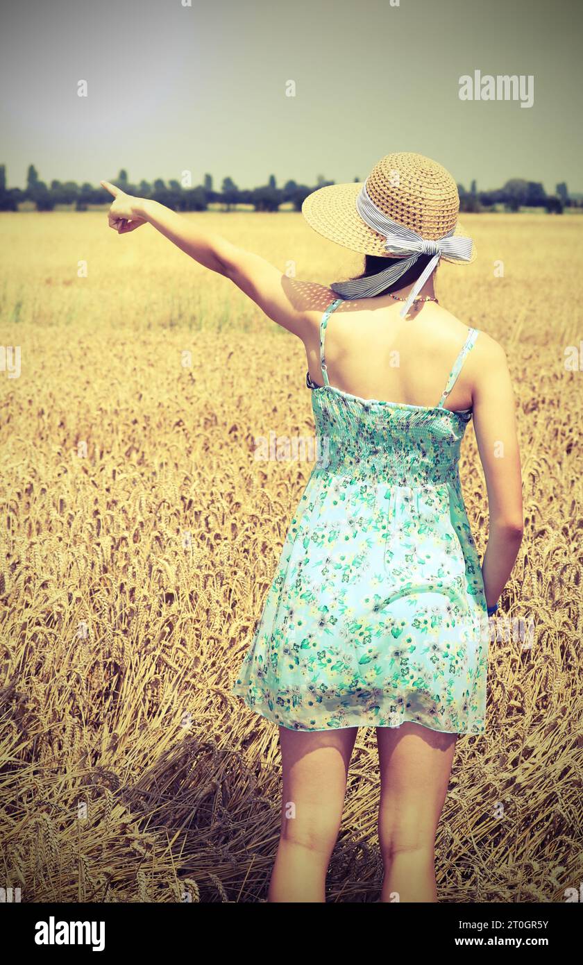 girl with straw hat in the wheat field  pointing to a nearby place with the index finger and antiqued toned effect Stock Photo