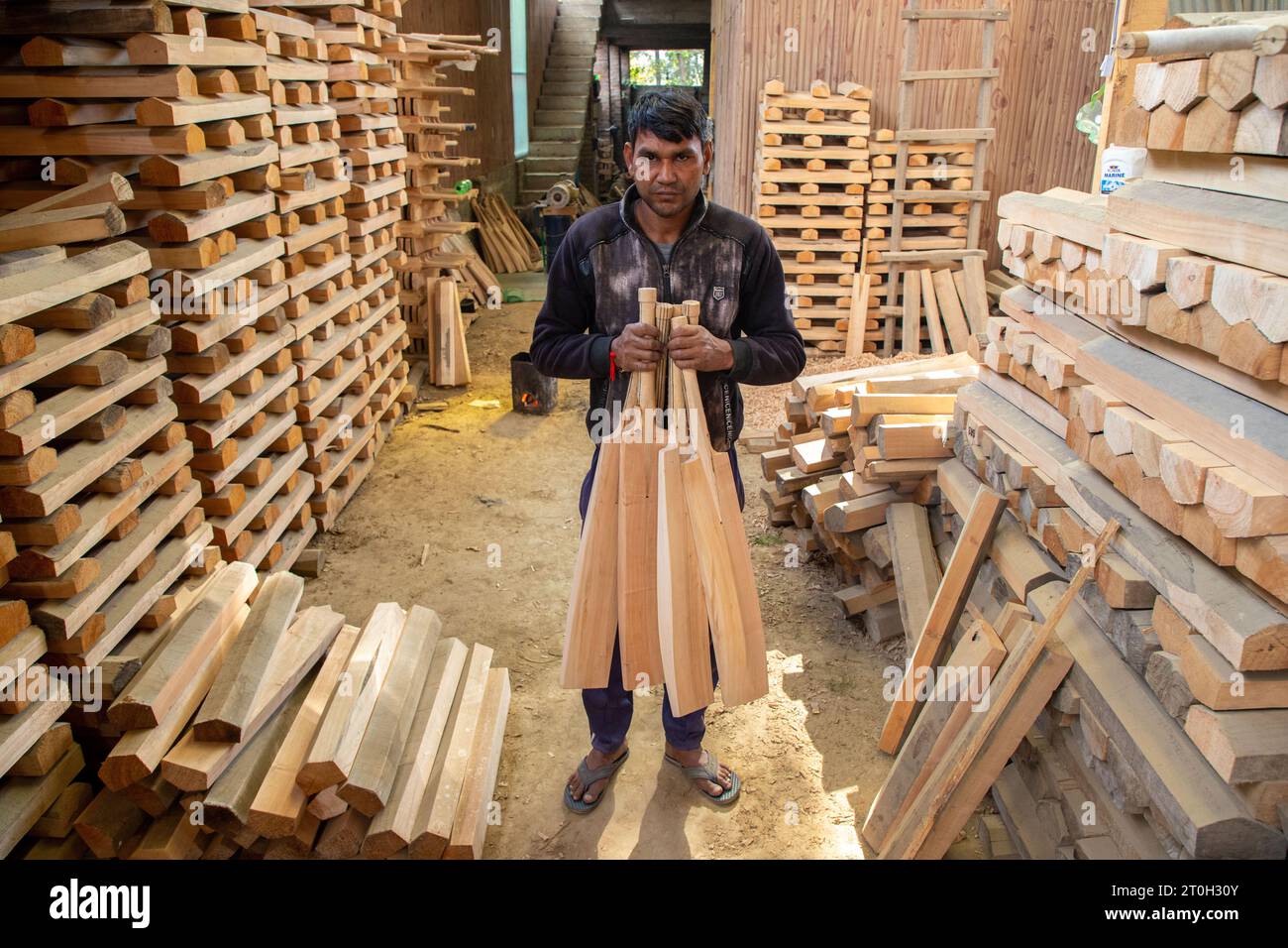 A worker carrying finished Kashmiri willow wood cricket bats at a