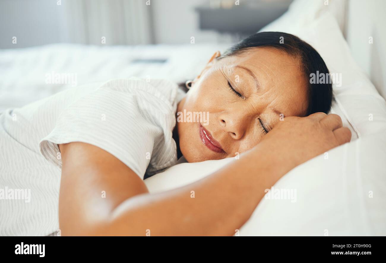 Mature, woman and calm while sleeping in bed with good dream, head on pillow and peace. Asian, elderly person and face in bedroom, alone and smile Stock Photo