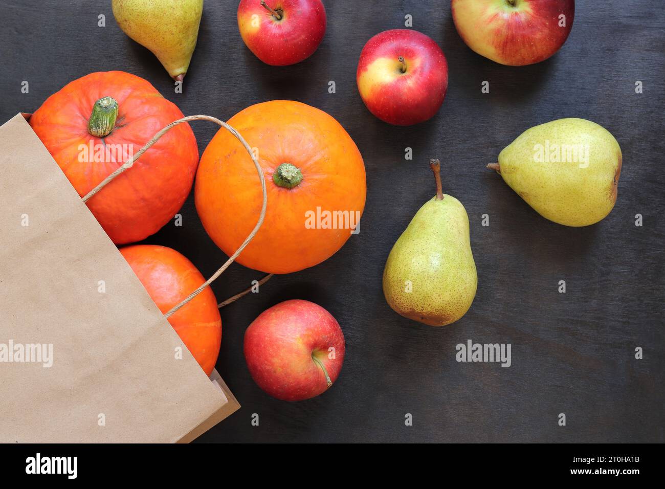 Kraft bag and fruits and vegetables on the table. Thanksgiving and Autumn design concept. Autumn background with ripe pumpkins, apples and pears on a Stock Photo
