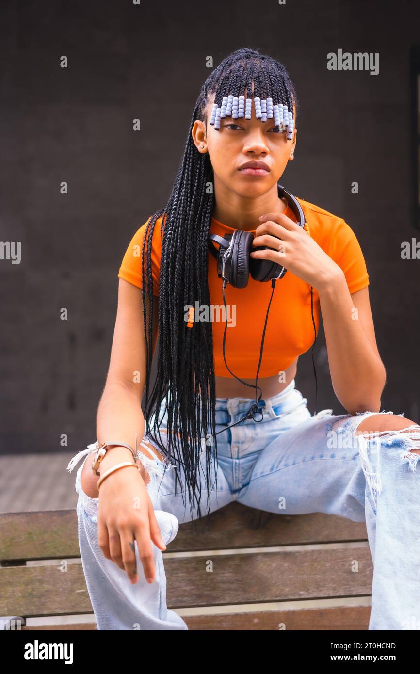 Lifestyle with a young trap dancer with braids in the city. Black Race Girl African Ethnicity With Orange T-Shirt And Cowboy Pants, Vertical Photo Stock Photo