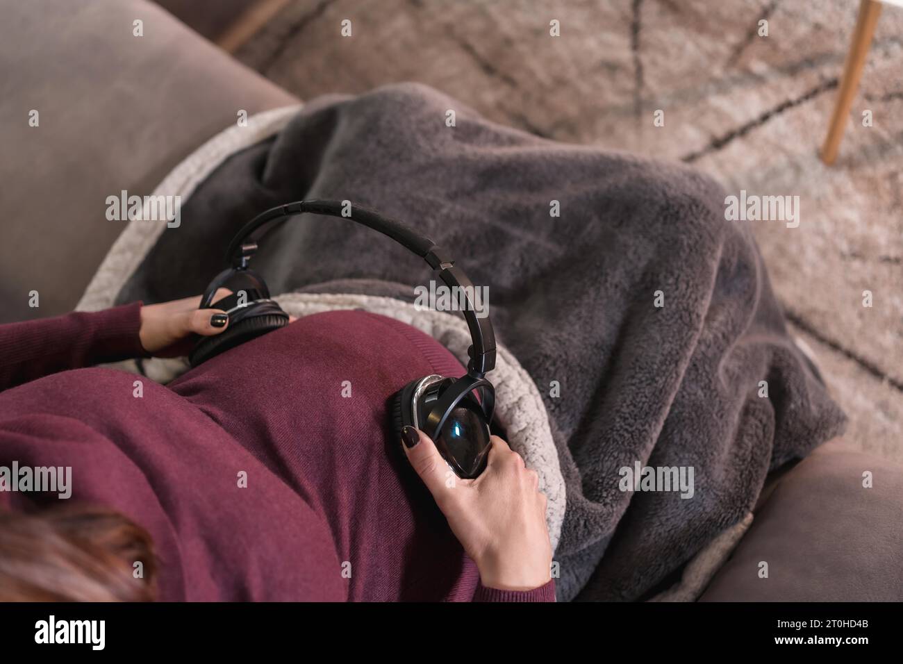 Detail of a young pregnant woman connecting with the child putting music with headphones, in the well-being of her home Stock Photo