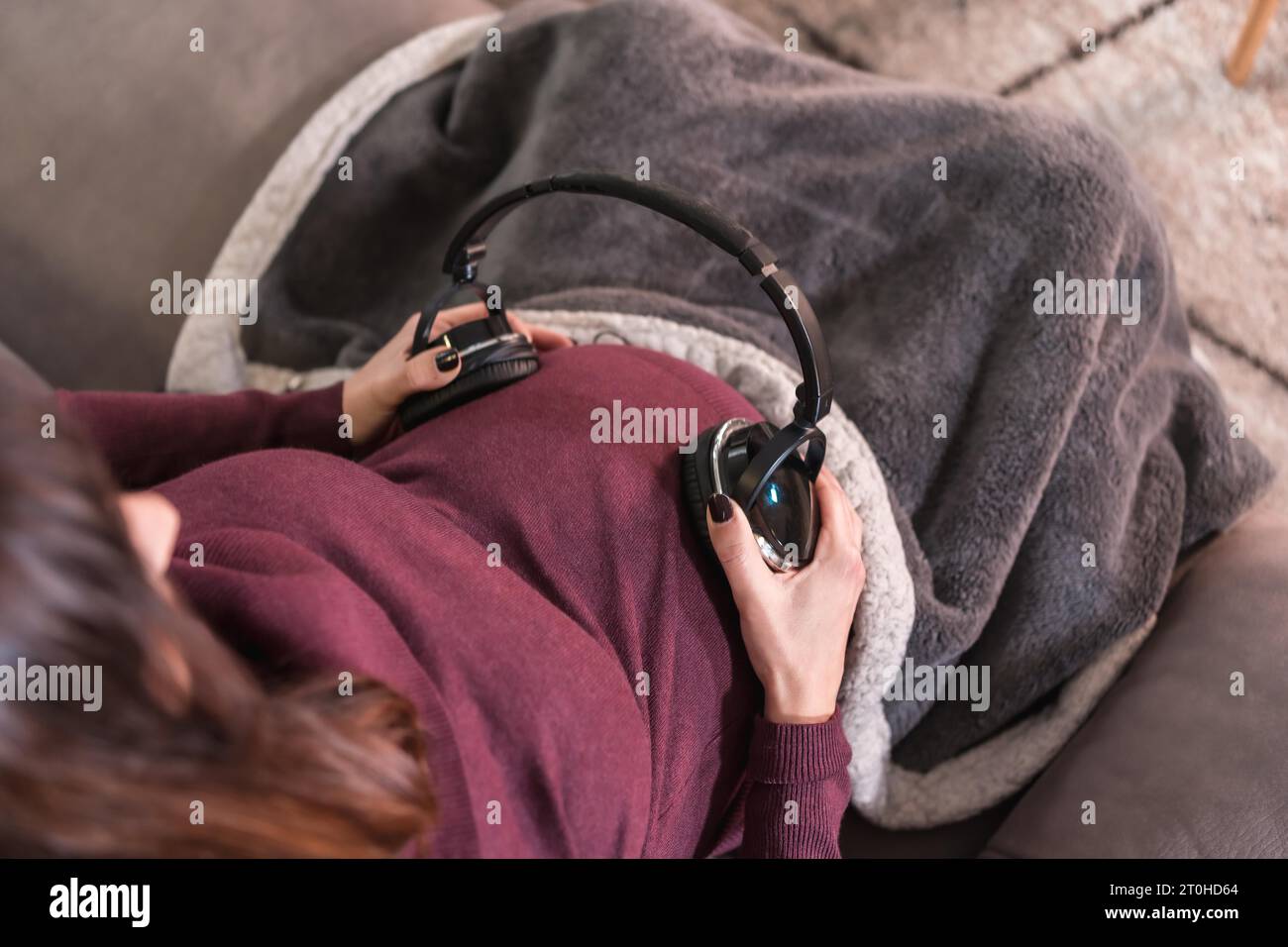 Detail of a young pregnant Caucasian woman connecting with the child putting music with headphones, in the well-being of her home Stock Photo