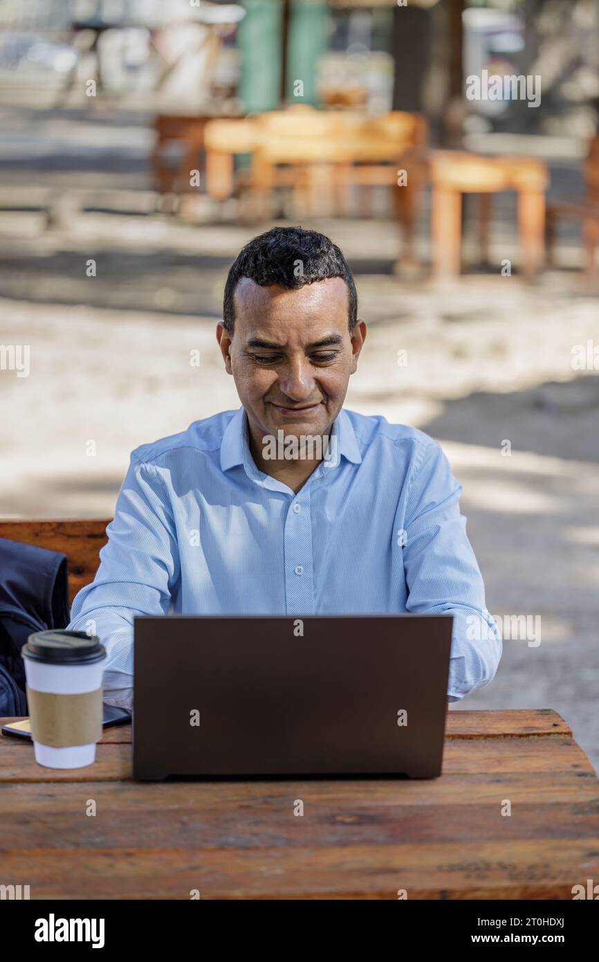 Latin man using laptop at outdoor bar table. Stock Photo