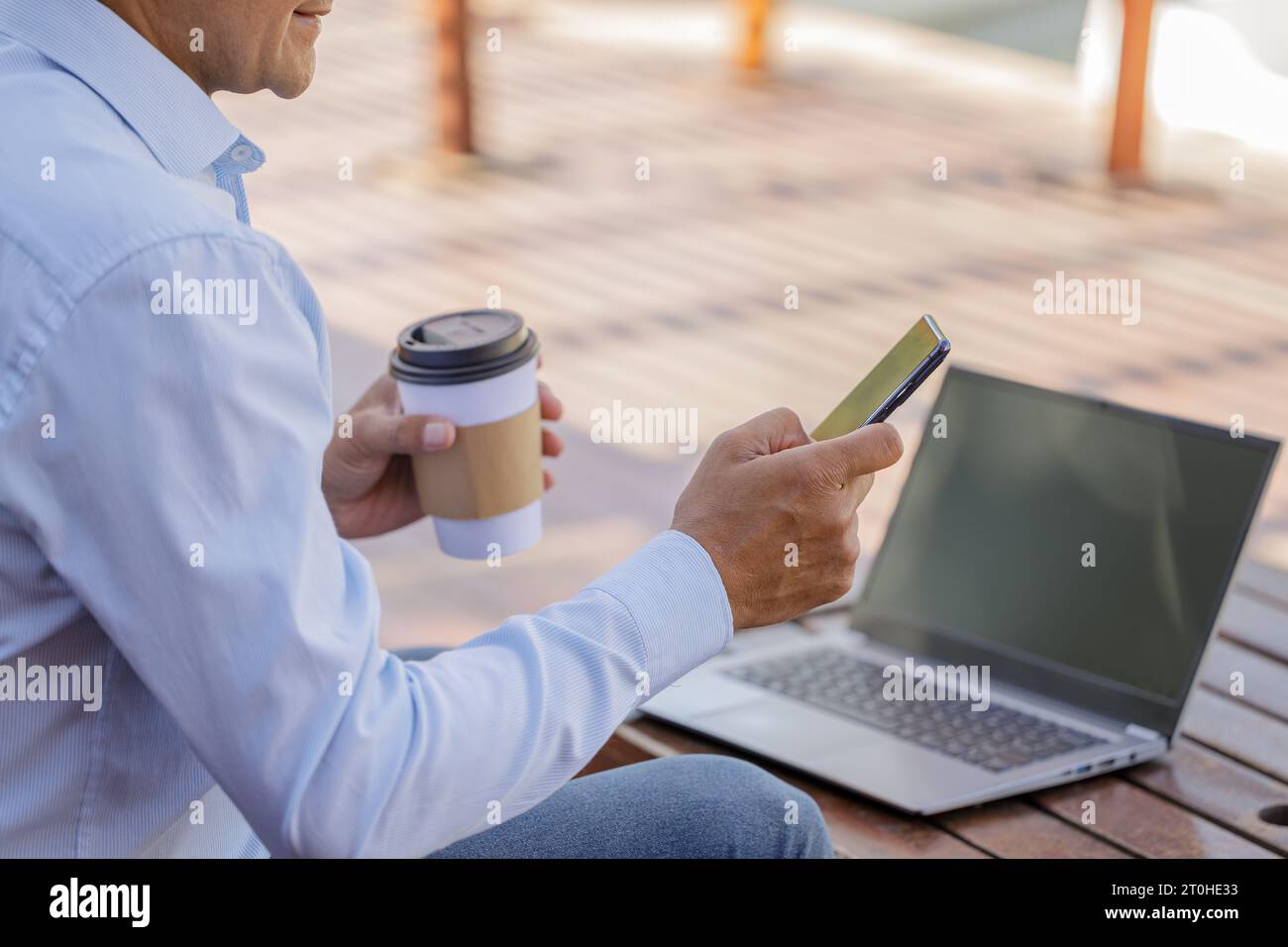 Detail of the hands of a Latin man holding a mobile phone in front of a laptop. Stock Photo