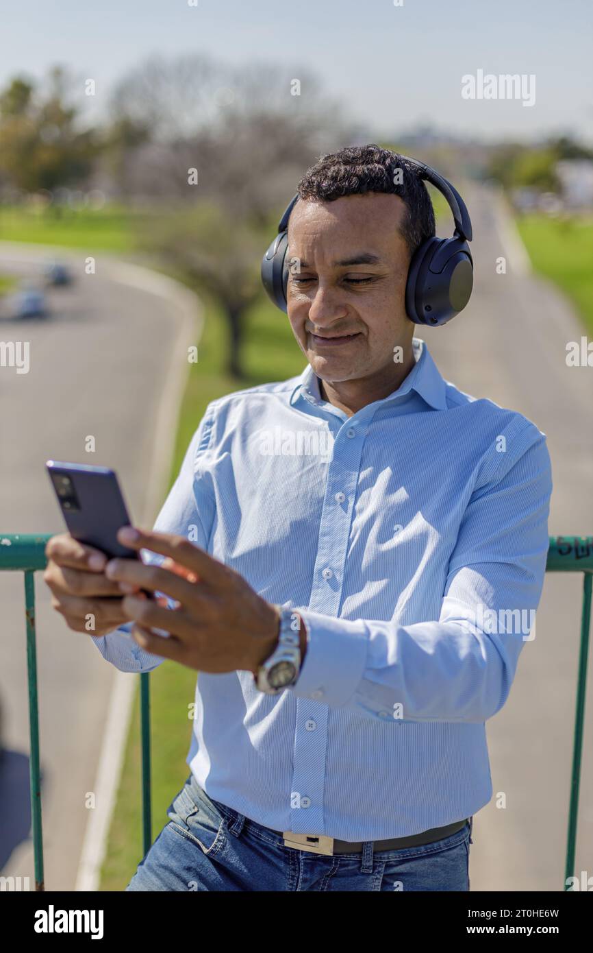 Latin man with headphones using his mobile phone on a pedestrian bridge. Stock Photo