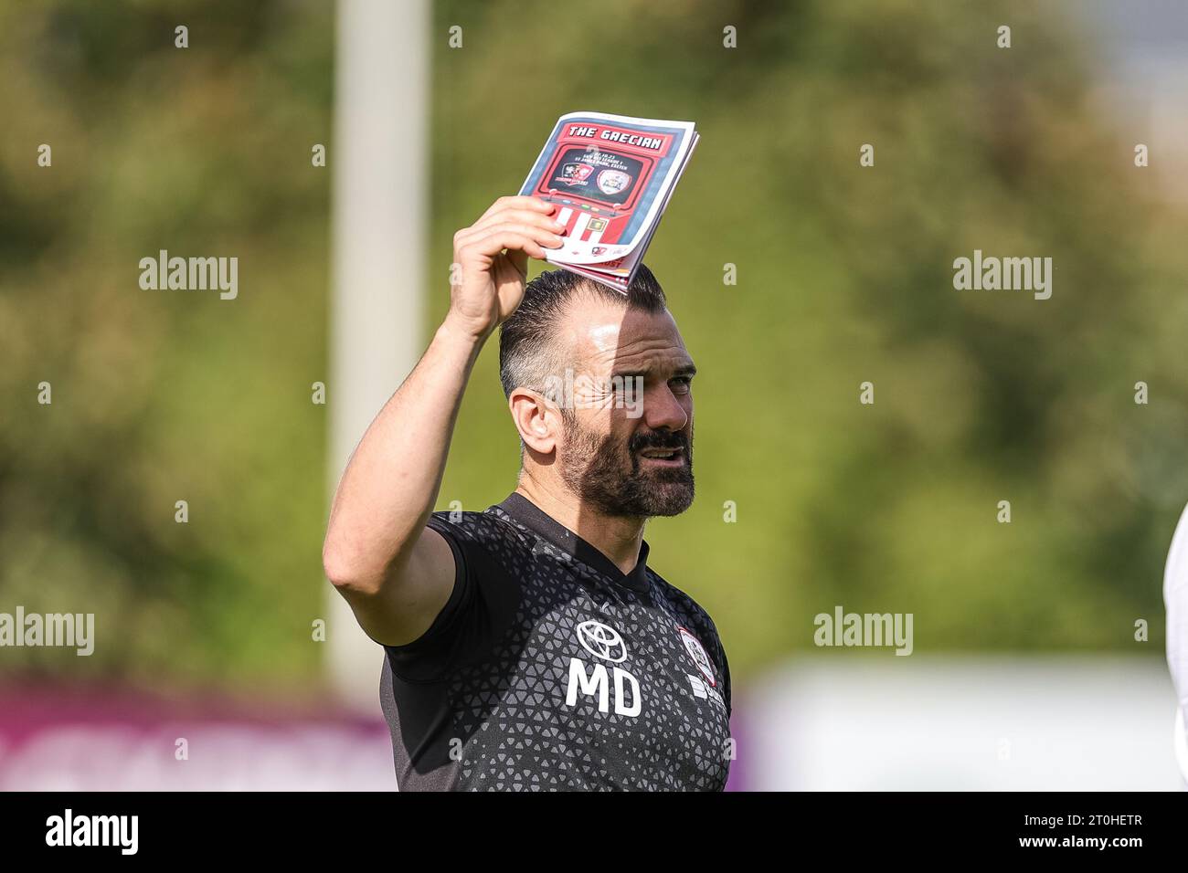 Martin Devaney first team coach of Barnsley   blocks the sun with todays match day program during the Sky Bet League 1 match Exeter City vs Barnsley at St James' Park, Exeter, United Kingdom, 7th October 2023  (Photo by Mark Cosgrove/News Images) Stock Photo