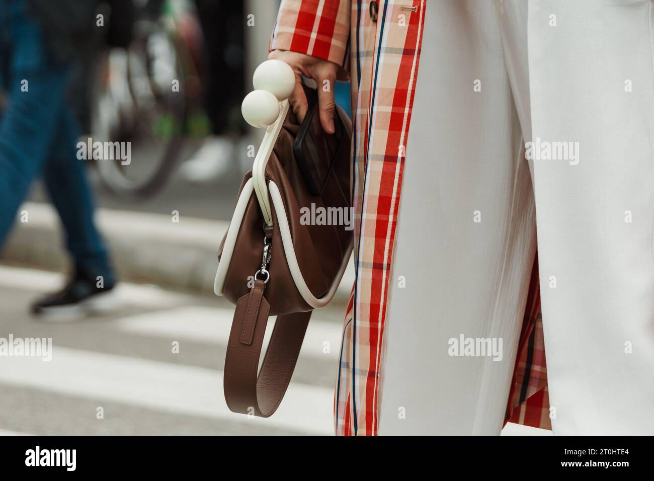 A guest wearing a checkered trench coat, white pants, a tie and brown bag, seen outside PRADA show during Milan Fashion Week Womenswear Spring/Summer Stock Photo