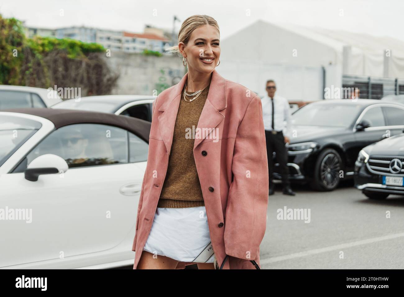 Emili Sindlev wears necklaces, a knit pullover, a pink suede oversized jacket, Prada bag, seen outside PRADA show during Milan Fashion Week Womenswear Stock Photo