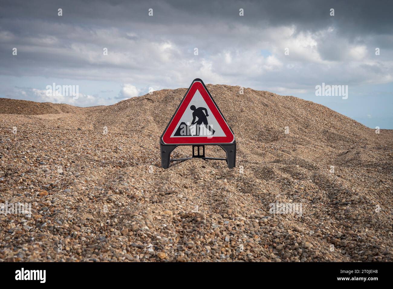 Large pile of shingle with a 'men at work' sign in the foreground Stock Photo