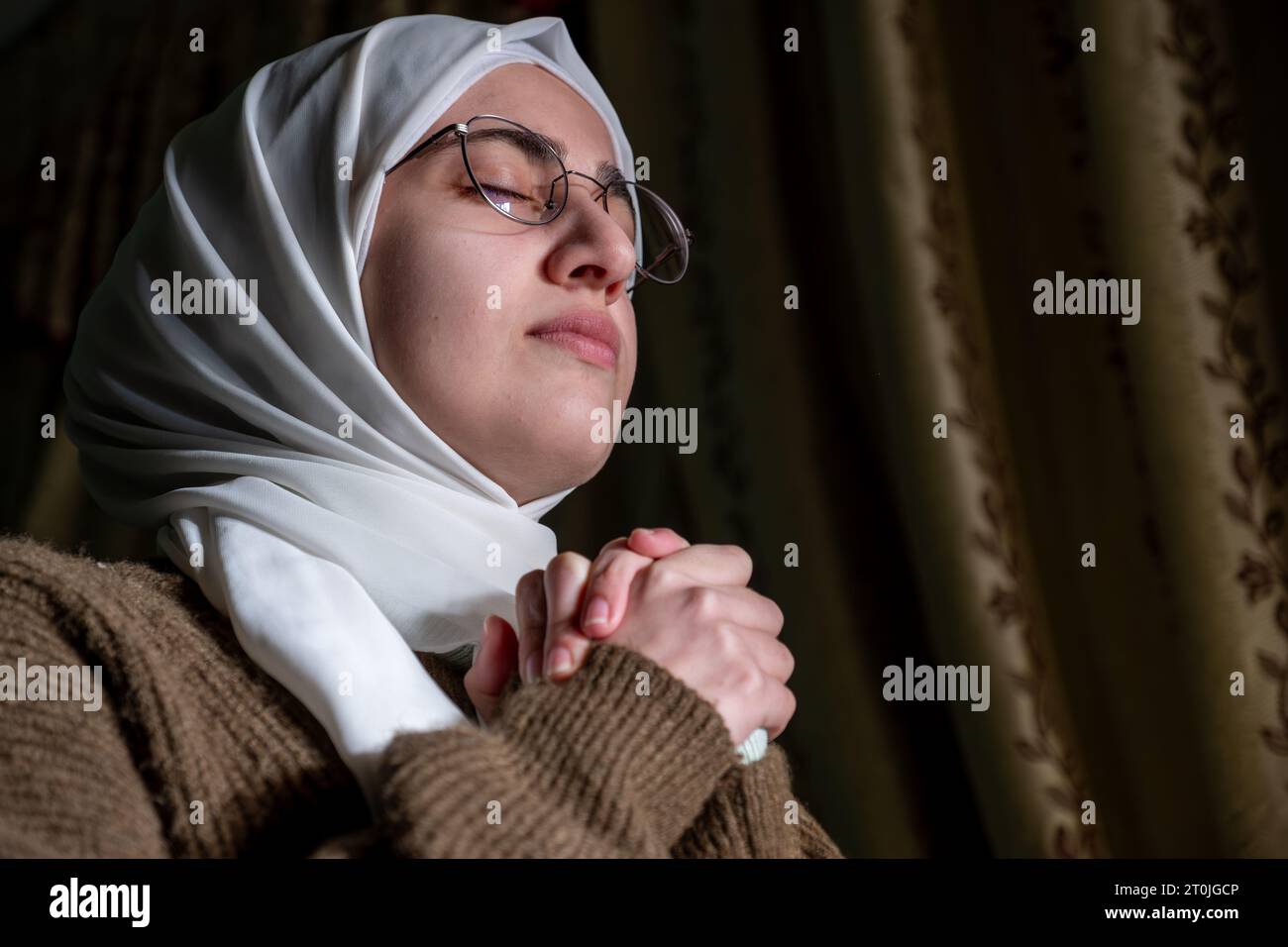 A Muslim woman raises her prayers to God to remove the affliction and illness from her and to relieve her of the calamities that have befallen her Stock Photo