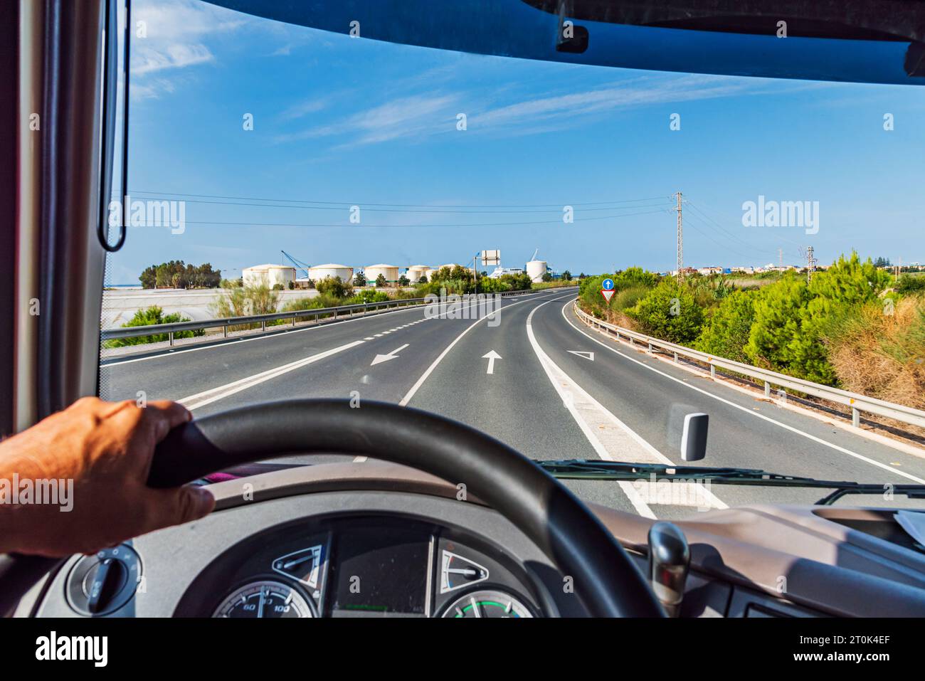 View from the driving position of a truck of a road that leads to some factory warehouses. Stock Photo