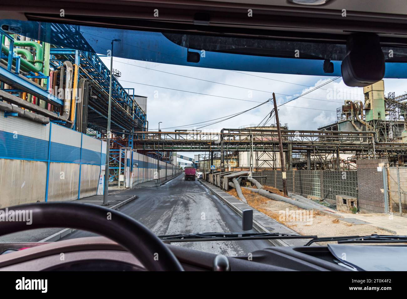 View from the driving position of a truck of a street that crosses between factories with pipes connected to each other. Stock Photo