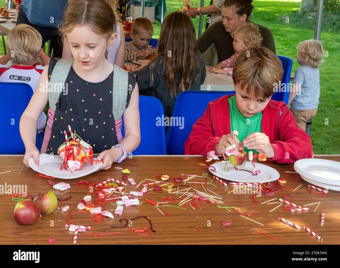 Kids children decorating apples with candy or sweets in a fun competition at Alresford Apple Day event, Hampshire, England, UK, October 2023 Stock Photo