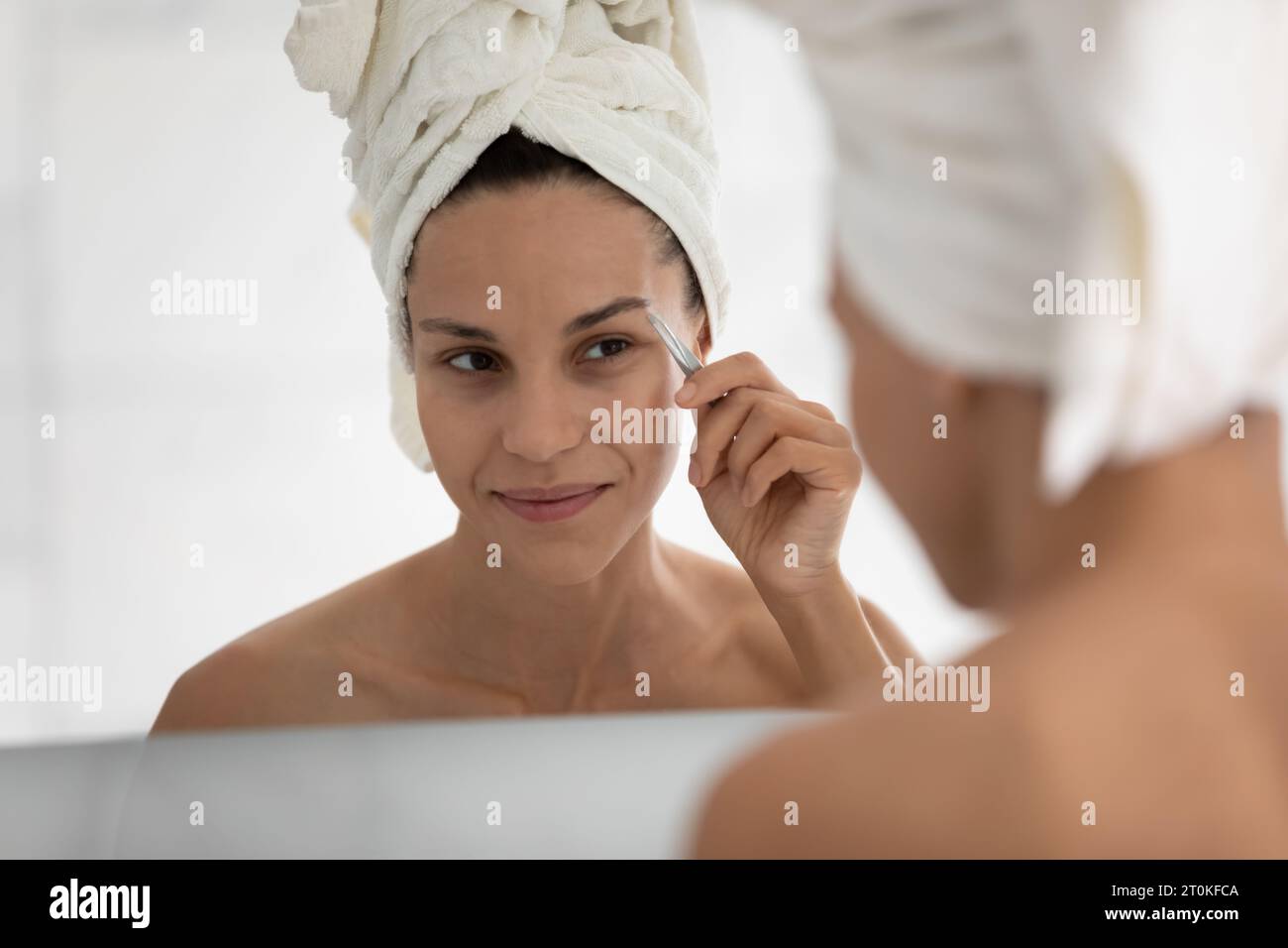 Young woman look in mirror pinch eyebrows in bathroom Stock Photo