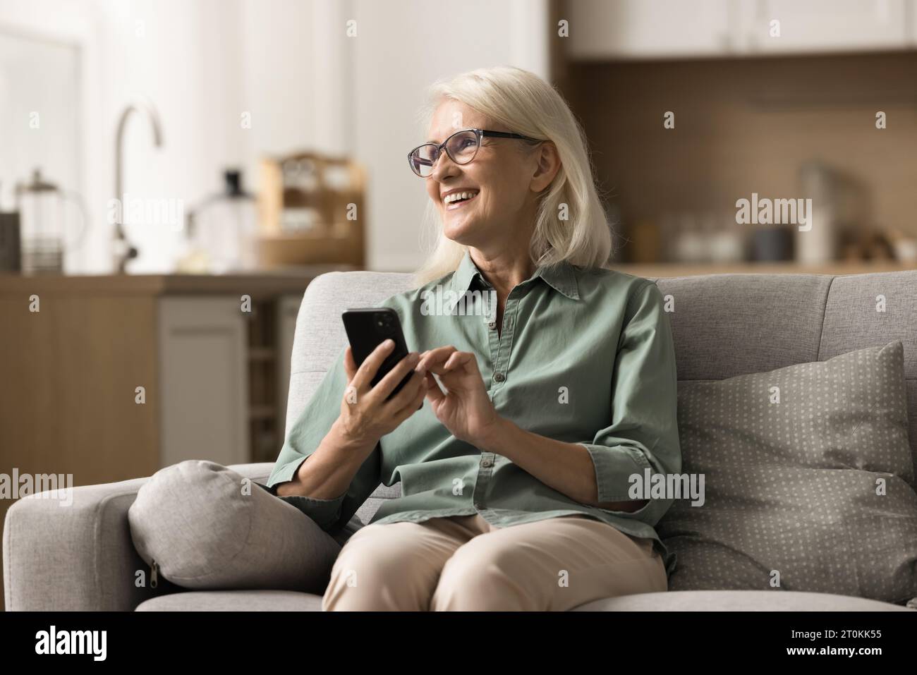 Happy positive older blonde woman in eyewear holding smartphone Stock Photo