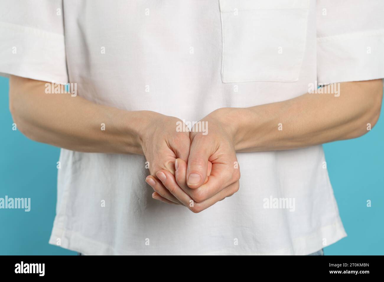 Woman cracking her knuckles on turquoise background, closeup. Bad habit