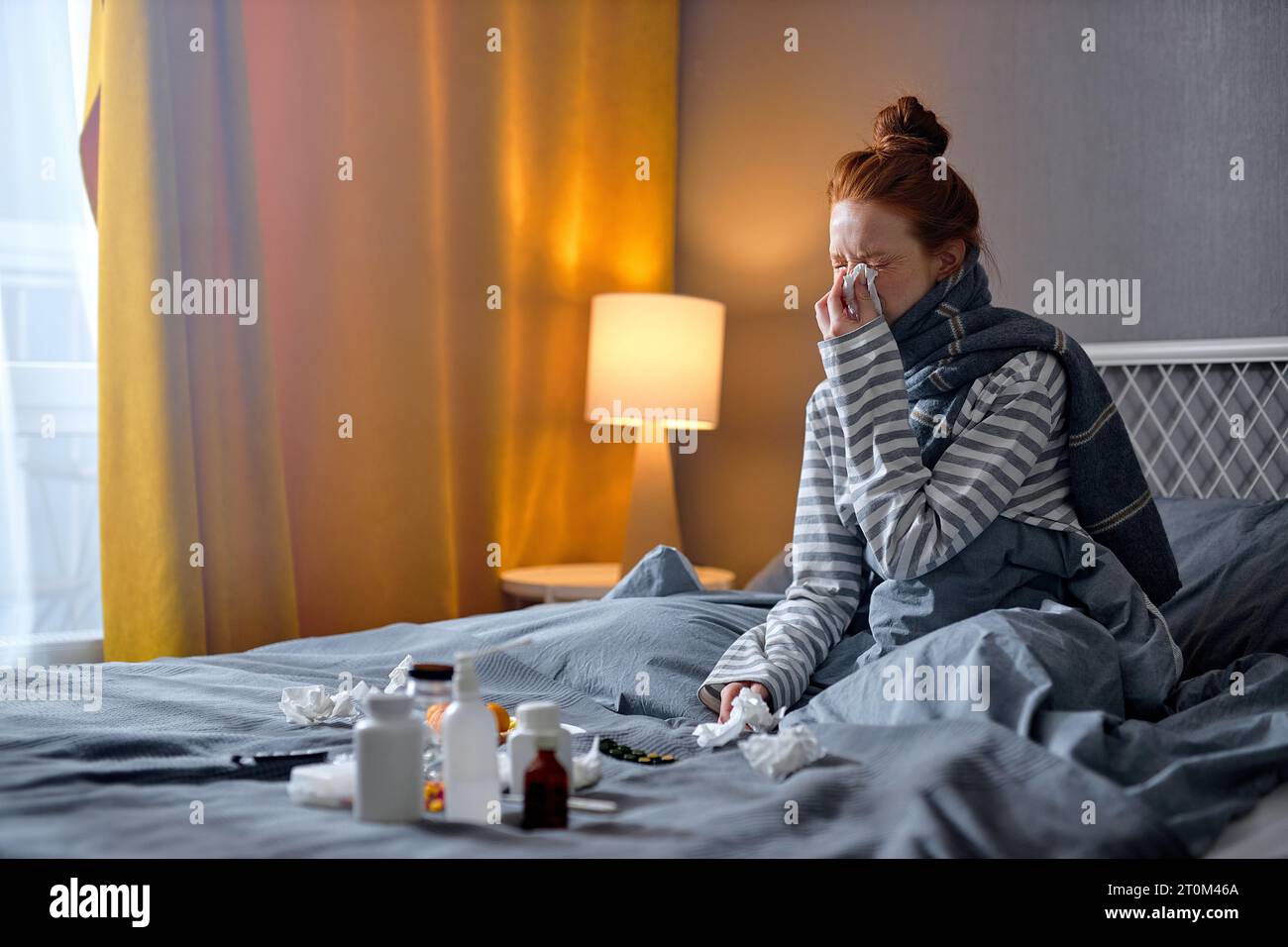 young redhead caucasian woman having cough, sneezing, feeling sick and lying on bed, take medicine in bedroom. ill female in warm clothes need medical Stock Photo