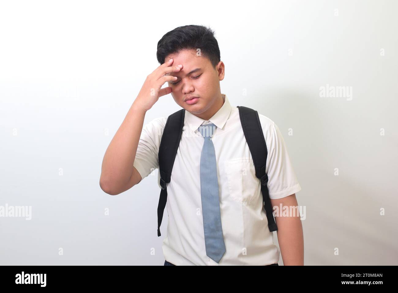 Indonesian senior high school student wearing white shirt uniform with gray tie suffering headache and holding hands on forehead. Isolated image on wh Stock Photo