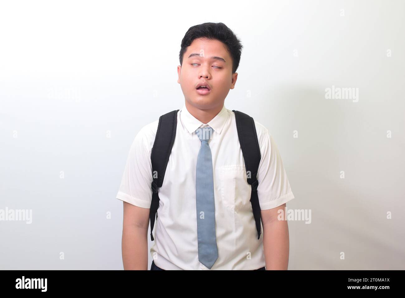 Indonesian senior high school student wearing white shirt uniform with gray tie yawning with closed eyes due to overworking. Isolated image on white b Stock Photo