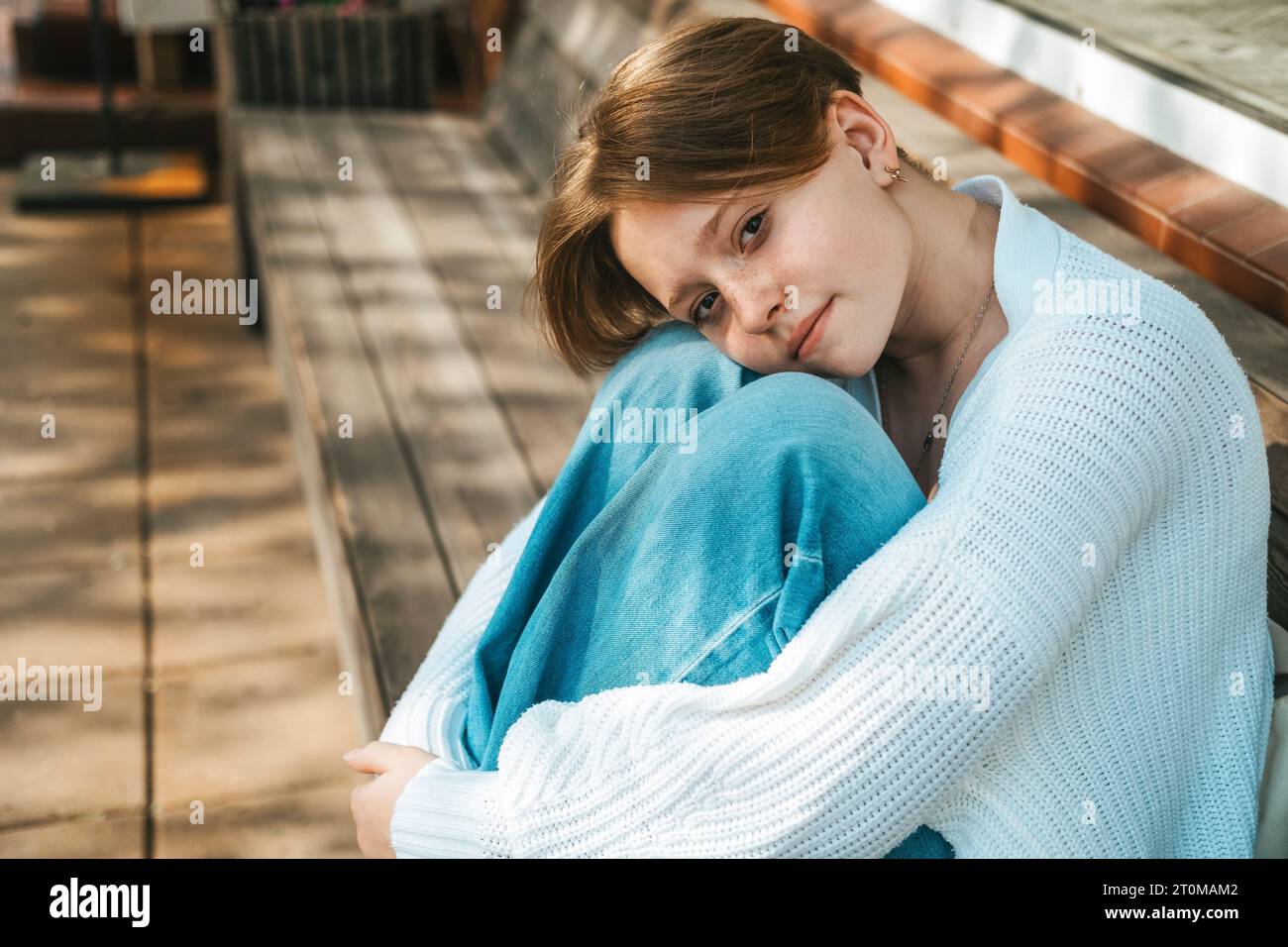 A teenage girl sits on a bench on the street, hugging her knees Stock ...