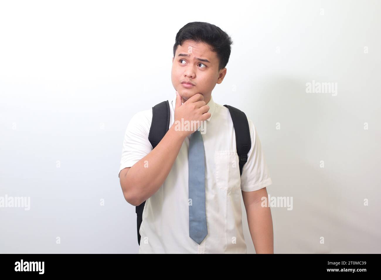 Indonesian senior high school student wearing white shirt uniform with gray tie and thinking about question with hand on chin. Isolated image on white Stock Photo